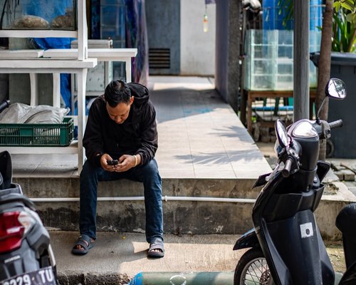 Indonesian urban commuter using smartphone near a bright window